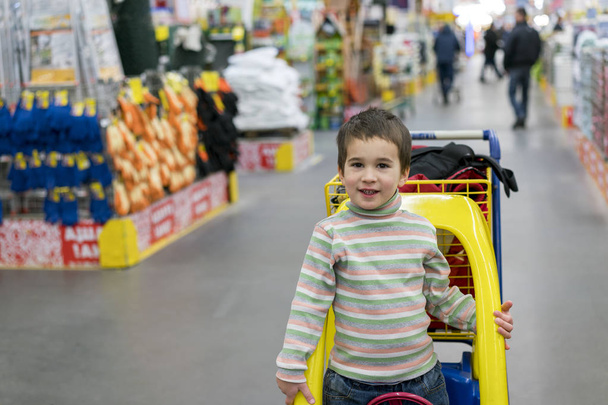 The boy 4 years leaned out of the children's cart in the building store. Dangerous behavior of children. - Photo, Image