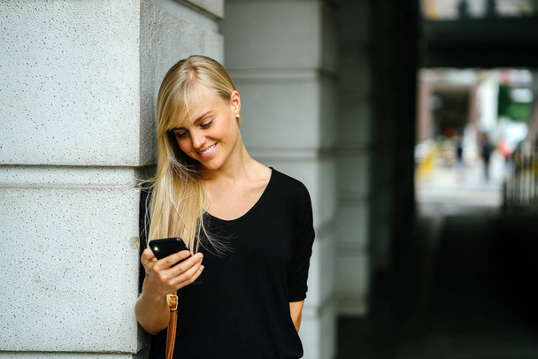 young and attractive blond woman tourist or exchange student is using her phone on a street in Asia during the day. - Фото, изображение