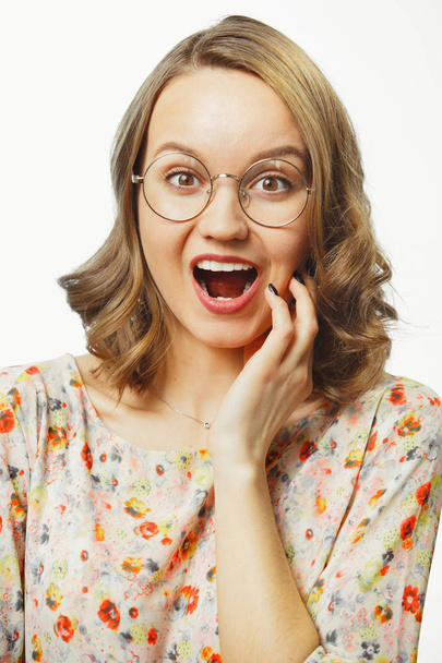 verticale close-up portret van een jonge vrouw met levendige emotie verrassing, geopende mond, ogen wijd open, spreekt verrassing en verwarring, draagt de ronde bril, geïsoleerd op wit. - Foto, afbeelding