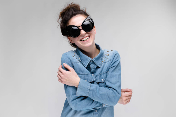 Young brunette girl in black glasses. Cat glasses. The hair is gathered in a bun. The girl folded her arms. The girl is laughing. - Photo, Image
