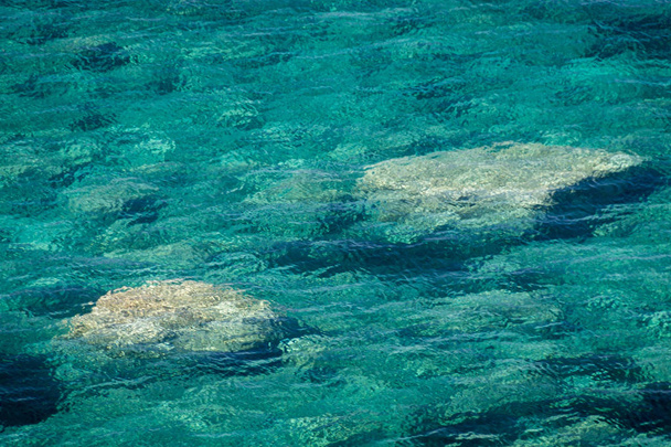 Textura de color esmeralda agua del océano con dos piedras que brillan a través de
 - Foto, imagen