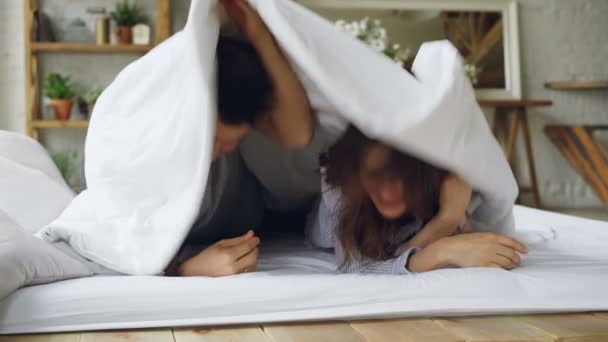 Portrait of happy couple lying in bed under blanket then showing faces looking at camera laughing and smiling. Loving married people and happiness concept. - Video