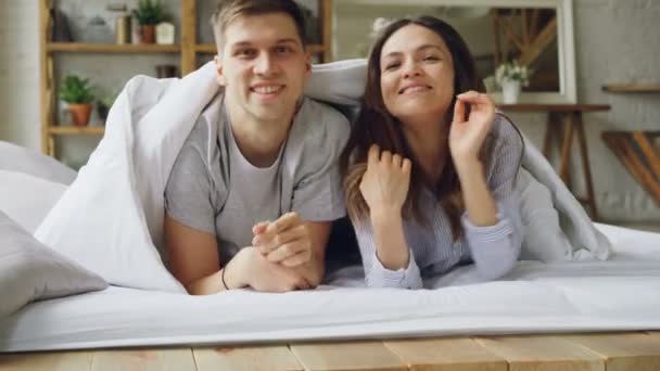 Portrait of happy mixed-race couple emerging from under the blanket, smiling and looking at camera. Happy married life, attractive people and relationship concept. - Video