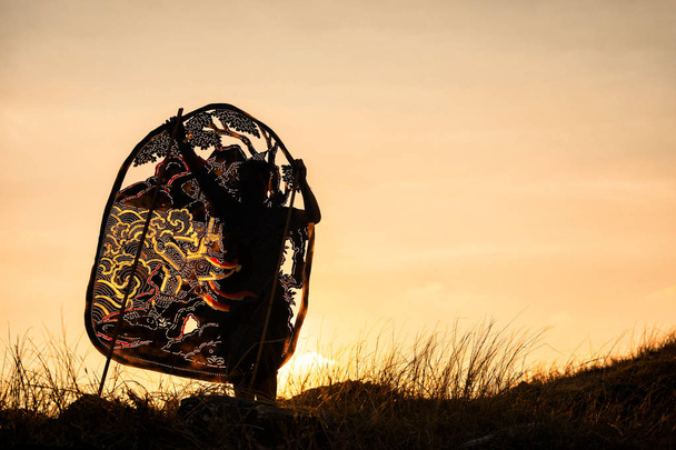 Silhouette artista uomo tenendo Thai shadow angel burattino a prato di montagna presentare durante il tramonto con spazio copia per il testo. Tradizionale Thailandia arte pari con sfondo crepuscolo naturale
. - Foto, immagini