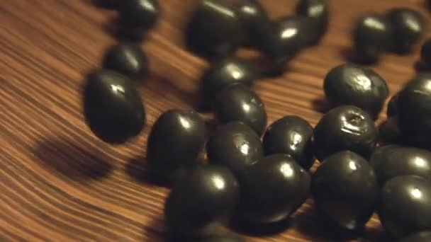 Black olives on a brown wooden background. 2 Shots. Slow motion. Close-up.1. Olives are rolling down ( from left to right ) on a brown wooden background and fills the all space frame.2. Vertical ( from top to bottom ) pan.  - Footage, Video