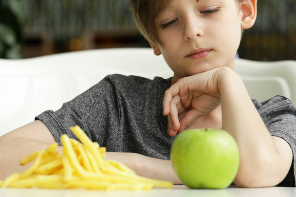 menino loiro bonito escolhe frutas ou fast food
 - Foto, Imagem