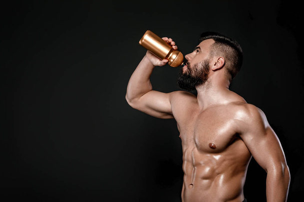 Handsome strong bodybuilder drinks water isolated on black background - Photo, image