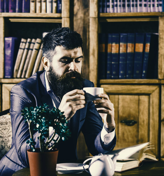 librarian to the library. Oldfashioned man holds cup with tea. Aristocratic lifestyle concept. - Foto, afbeelding
