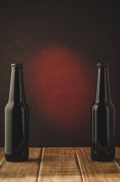 two black bottle of beer on a red background/two black bottle of beer on a red background.  Selective focus and copyspace - Φωτογραφία, εικόνα