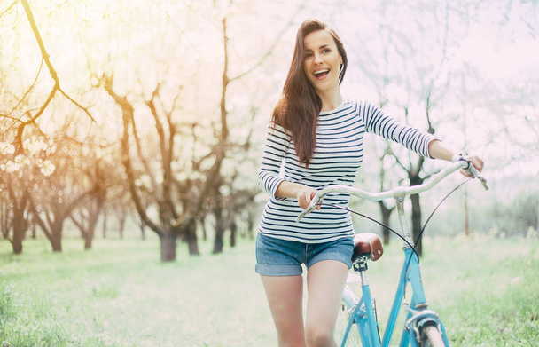Smiling young woman standing with bicycle on garden background - Fotoğraf, Görsel