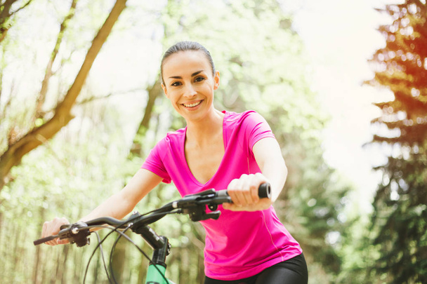 Smiling young caucasian woman riding sport mountain bicycle in forest - Foto, Imagem