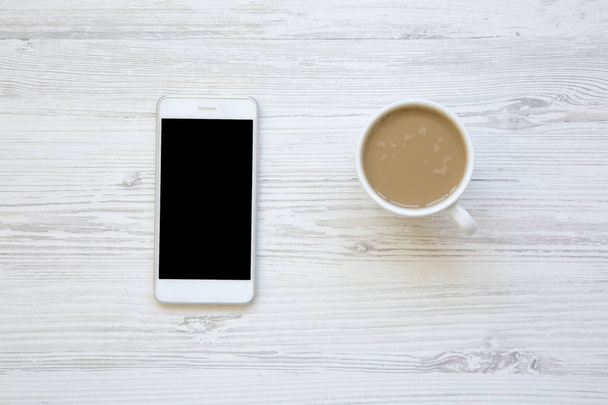 Smartphone mit Latte auf weißem Holzhintergrund, Draufsicht. - Foto, Bild