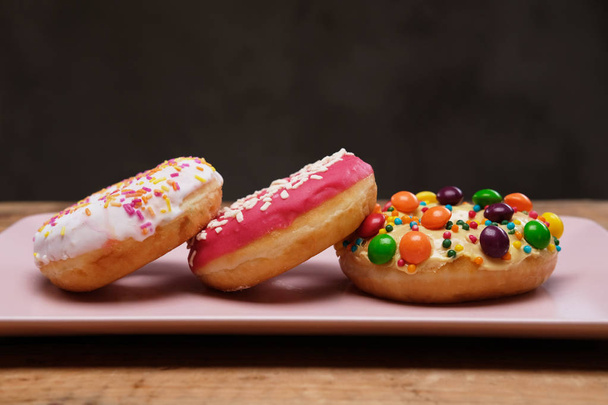 Три аппетитных пончика лежат на розовой керамической тарелке
. - Фото, изображение