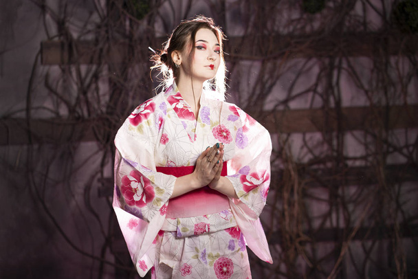 elegante Mädchen in einem klassischen traditionellen Kleid japanischen Kimono weiß und rosa allein stehend auf dunklem Hintergrund im Studio - Foto, Bild