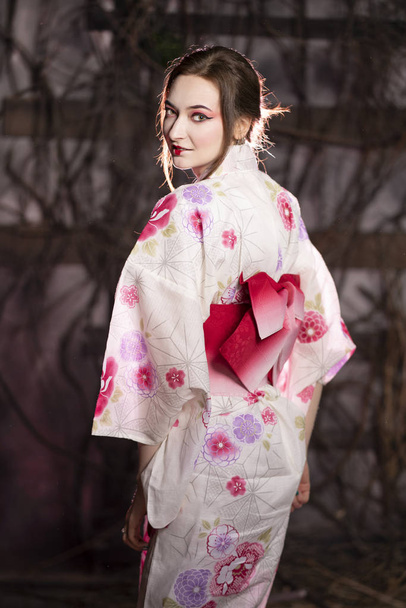 dziewczynka elegancki w klasyczny strój tradycyjny japoński kimono biały i różowy osamotniony na ciemnym tle w studio - Zdjęcie, obraz