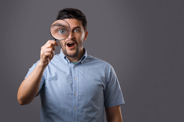 Young amazed bearded man with magnifying glass that enlarge his eye. Young guy searching - Fotoğraf, Görsel