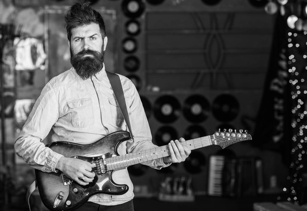 Musician with beard play electric guitar. Rock music concept. Man with strict face play guitar, singing song, play music. Talented musician, soloist, singer play guitar in music club on background - Photo, Image