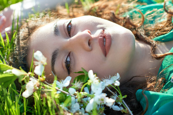 mooi meisje liggend op het gras op een zonnige dag, gezicht close-up, zomer bos, heldere landschap met schaduwen - Foto, afbeelding