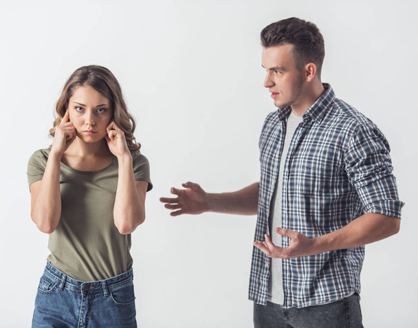 Una pareja joven tiene problemas. Chica está cubriendo sus oídos en su novio está hablando con ella, aislado en blanco
 - Foto, Imagen