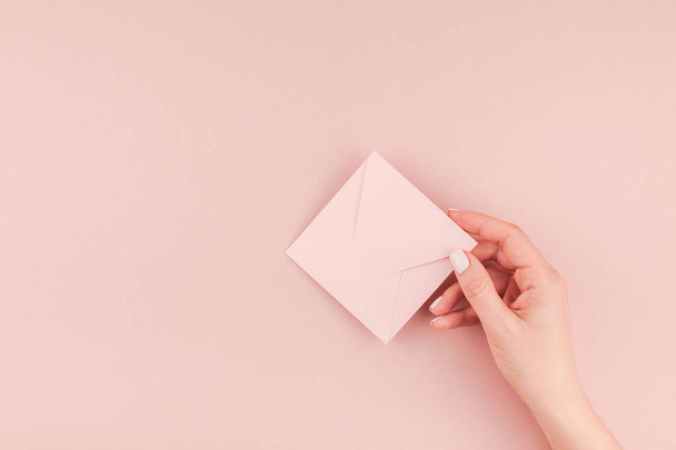 Creative image of woman hand holding small love letter with copy space on millennial pink background in minimalism style. Concept template for feminine blog, social media - Zdjęcie, obraz