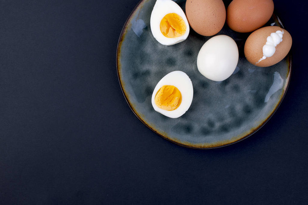 Boiled eggs on a plate and a black background. Fitness food, protein and yolk. Free space for text, copy space, flat lay - Фото, изображение