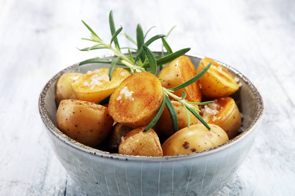 Patata asada con romero fresco en un bol sobre fondo rústico
 - Foto, imagen