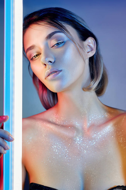 Sexy woman in neon light in lingerie. Neon lights and glare of light on the girl's face. Naked woman in sequins on the background of bright contrast light. Blonde with beautiful makeup on her face - Foto, imagen