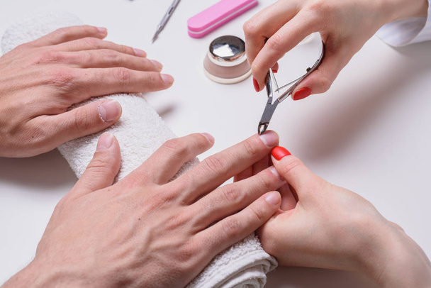 Mannen manicure. vrouw schoonheidsspecialiste behandelt nagelriemen van droge mannelijke handen. - Foto, afbeelding
