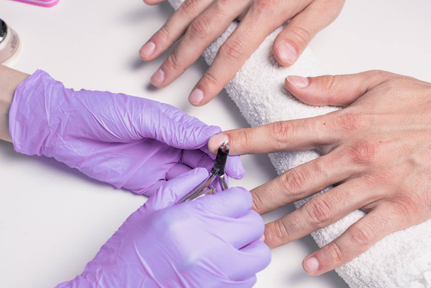 Mannen manicure. Schoonheidsspecialist in rubberen handschoenen snijdt nagelriemen op mannen handen. - Foto, afbeelding