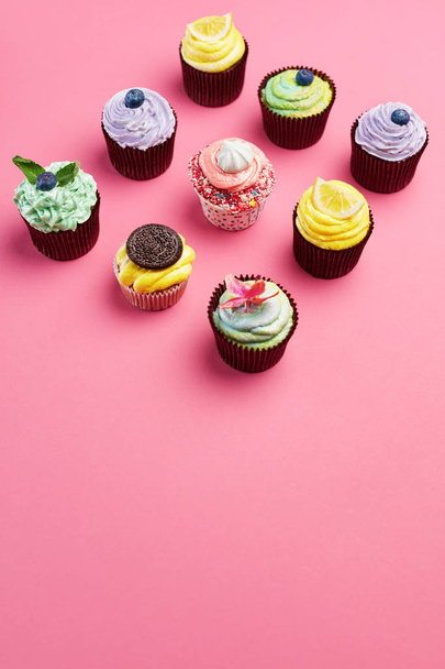 Kleurrijke Cupcakes op roze achtergrond. De Desserts van de cake met slagroom en verschillende Toppings. Hoge resolutie - Foto, afbeelding