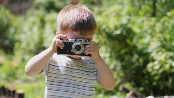 Portrait of a lovely little boy taking pictures outdoors on the vintage camera. Slow motion shot - Footage, Video