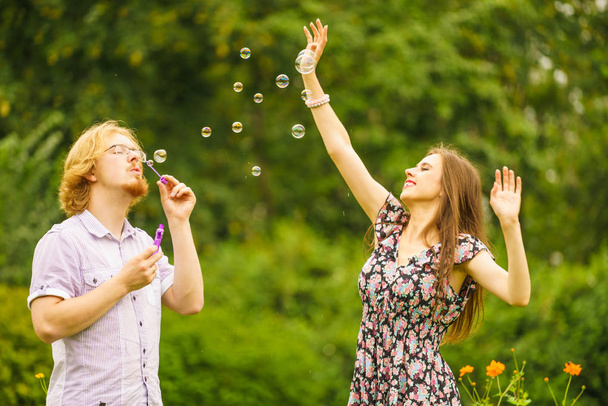 Happy funny hipster couple playing together blowing soap bubbles outdoor in spring park. - Foto, Bild
