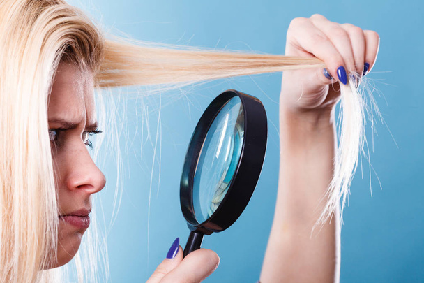 Haircare and hairstyling, bad effects of bleaching concept. Blonde woman looking at her damaged, split hair ends through magnifying glass. - Φωτογραφία, εικόνα