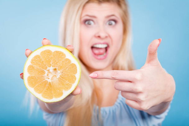 Woman smiling girl holding half of green yellow grapefruit citrus fruit in hand, pointing with finger, recommending healthy eating, on blue. Dieting losing weight concept. - Photo, image
