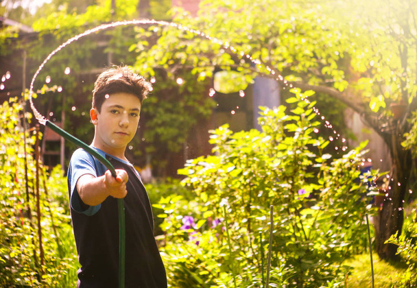Kinderhände halten Schlauch mit Spritzwasser auf dem sommerlich sonnigen grünen Garten - Foto, Bild