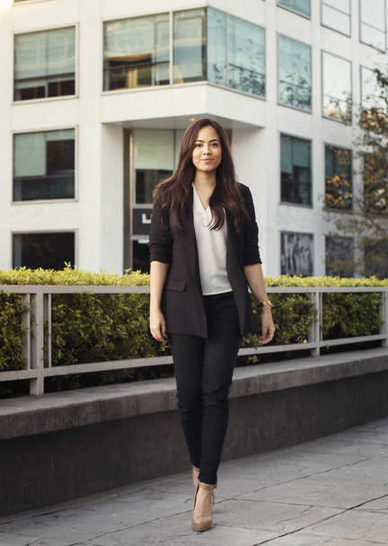 Beautiful hispanic business woman in suit walking at the street in a beautiful business quarter, vertical  - Photo, Image