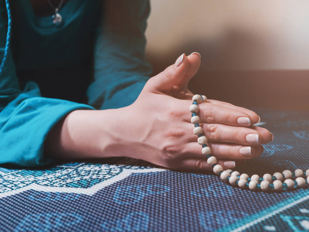 Concentrated woman praying with wooden rosary beads on yoga mat with mandala. Namaste. Close up hands. gratitude concept. - Foto, Bild
