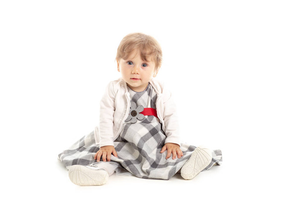 Élégant Bébé fille heureuse 1 an assis sur le sol du studio. Un fond blanc. Concept Bonheur
. - Photo, image
