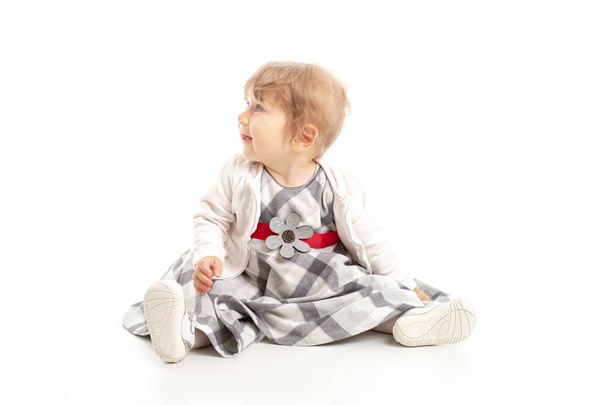 Elegáns boldog baba lány 1 éves a Műterem-padlón ül. Fehér háttér. Boldogság koncepciója. - Fotó, kép