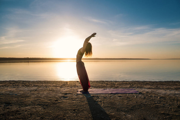 Sylwetka joga kobieta na plaży o zachodzie słońca. - Zdjęcie, obraz