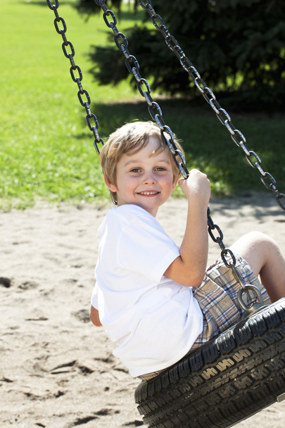 boční pohled na chlapce, houpající se na pneumatiku swing - Fotografie, Obrázek