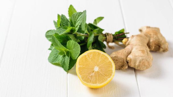 Ginger root, lemon, and a bunch of mint on a white wooden table. The composition of the ingredients to make a refreshing drink. - Fotoğraf, Görsel