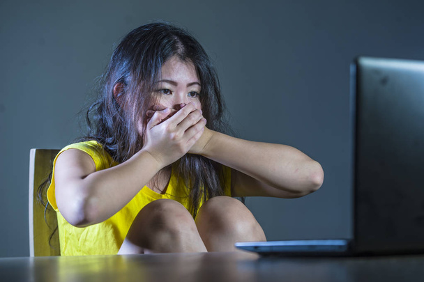 dramatic portrait of scared and stressed Asian Korean teenager girl or young woman with laptop computer suffering cyber bullying stalked and harassed with internet social media password hacked - Fotografie, Obrázek