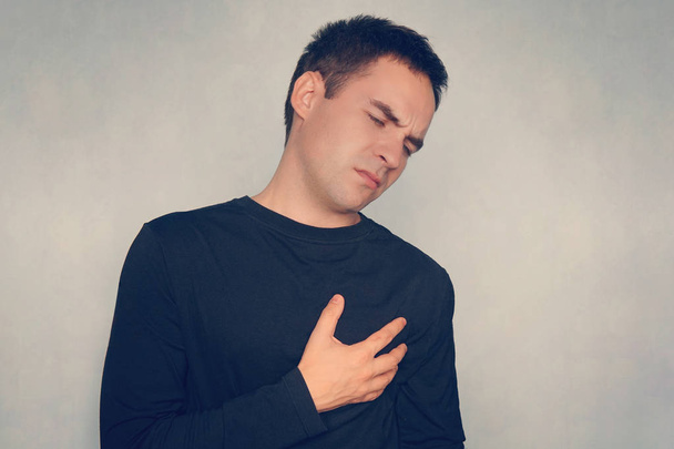 ο άνθρωπος υποφέρει από πόνο στο στήθος, καρδιακή προσβολή ή επώδυνες κράμπες, πατώντας πάνω στο στήθος με επώδυνη έκφραση. - Φωτογραφία, εικόνα