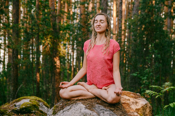 girl-yogi with pigtails sitting in Lotus position on a large stone in the forest in the summer - Valokuva, kuva