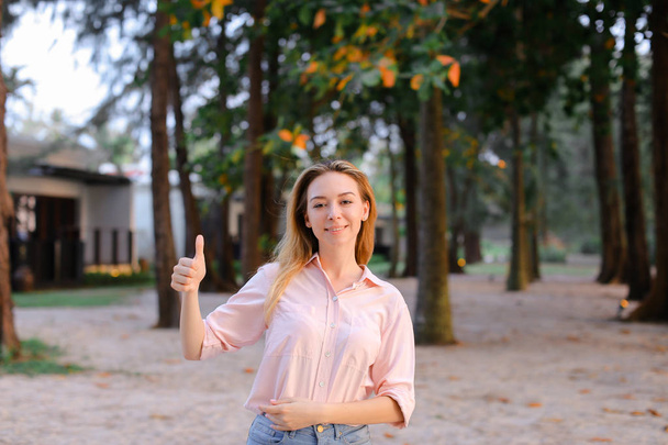 Mladá dívka stojí venku, stromy v pozadí, ukazuje palec. - Fotografie, Obrázek