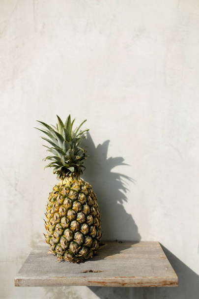 Mooie ananas staande op de plank, grijze muur op achtergrond. - Foto, afbeelding