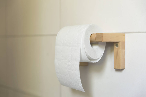 Een wit broodje voor zachte wc-papier netjes opknoping op een moderne houten houder op een witte tegels badkamer muur. - Foto, afbeelding