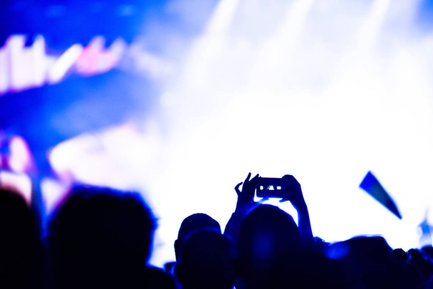 Ihmiset ottavat valokuvia kosketuksella älypuhelimeen musiikkikonsertin aikana. Kirkkaat näyttämövalot
 - Valokuva, kuva