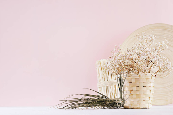 Small white dried flowers in beige wicker basket and wooden decor on soft pink pastel background. - Foto, Bild